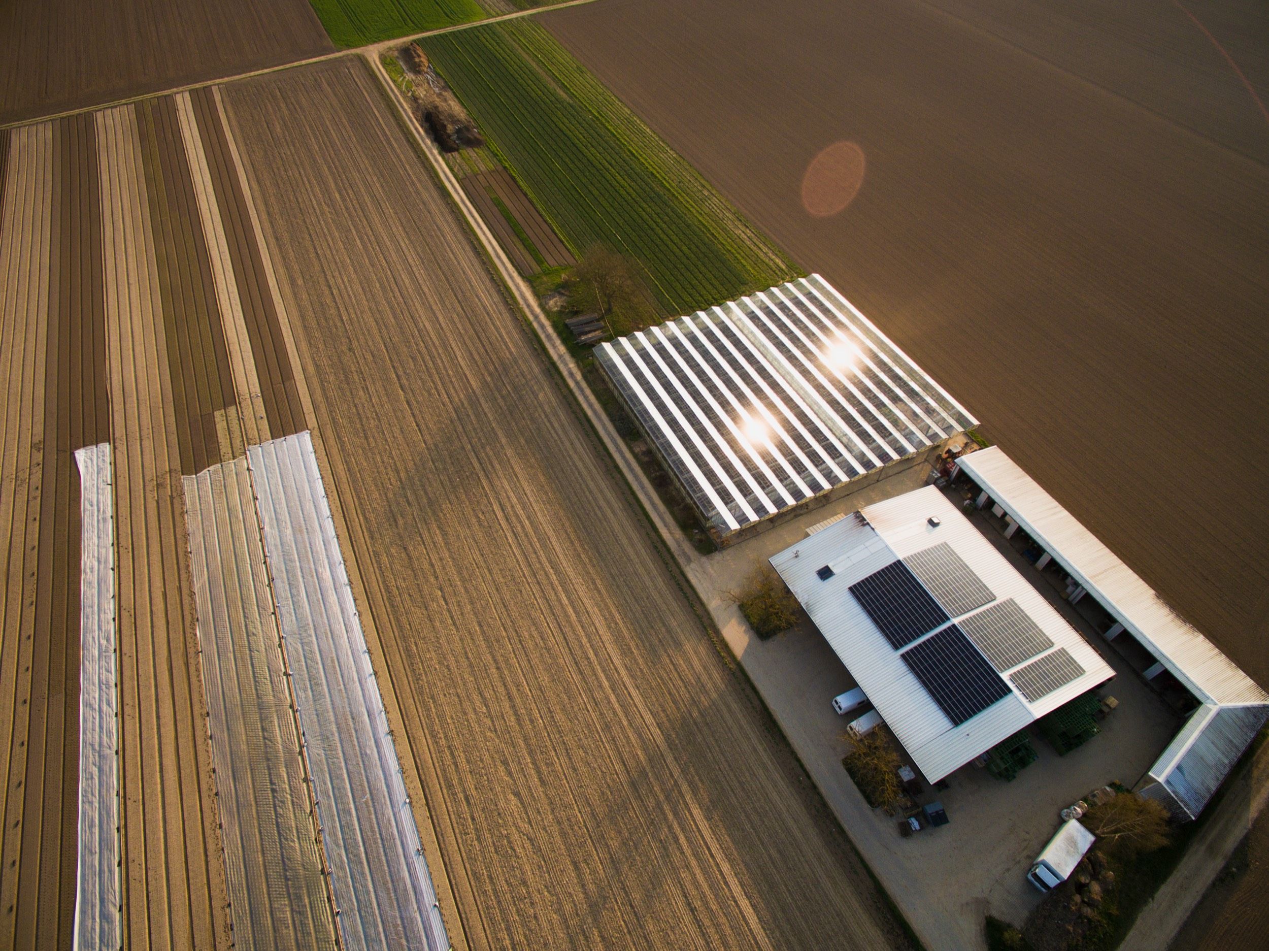 Luftaufnahme eines Hauses mit Solarmodulen, einem Gewächshaus und umgebenden Feldern