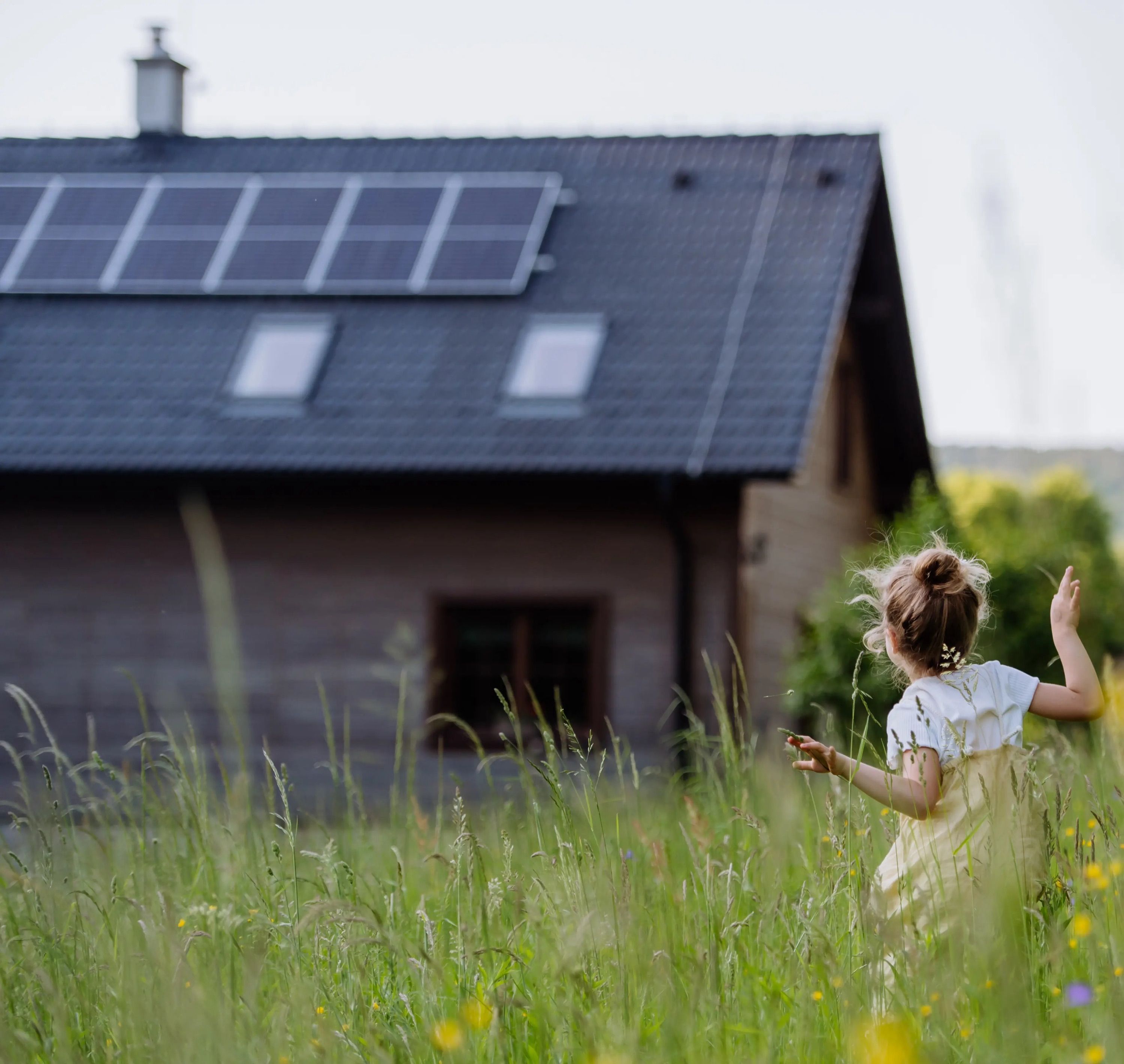 Kind von hinten vor Haus mit Photovoltaik-Anlage